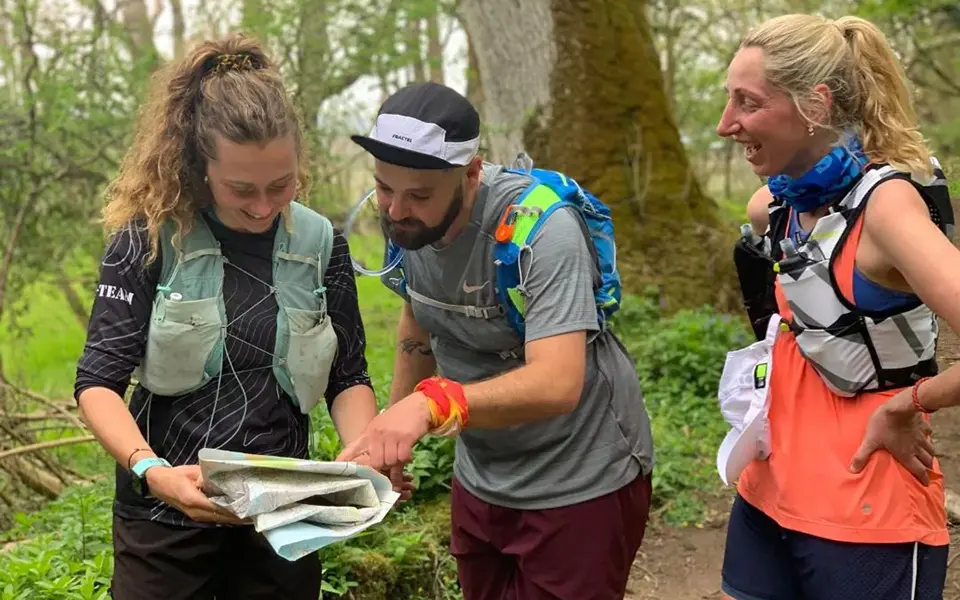 Lauren teaching a couple basic navigation techniques during a beginners' course, standing outdoors with maps and compasses.