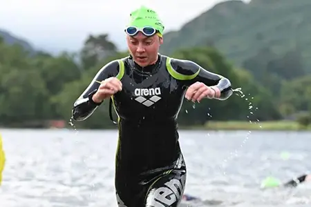 Lauren, wearing a swimsuit and goggles, emerges from the water during a challenging open-water swimming race set against the stunning backdrop of the Lake District.