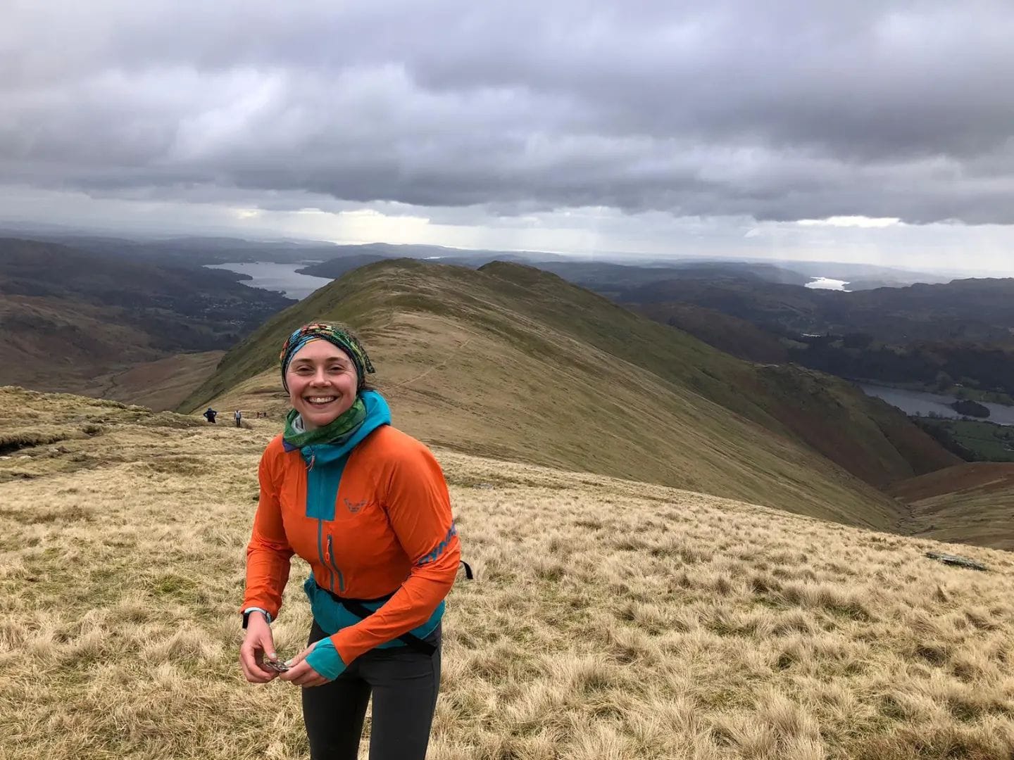 Lauren smiling on a mountain with lakes in the background. Lauren is holding a snack she is about to eat.
